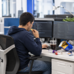 Programador en su escritorio consume comida basura y snacks poco saludables frente al ordenador, ilustrando los malos hábitos que provocan problemas de salud y absentismo laboral en empresas.